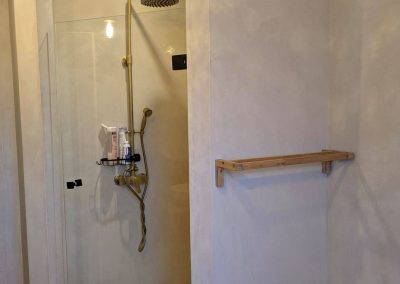 Douche moderne à garnerans avec béton ciré, paroi vitrée, robinetterie dorée mate et ambiance douce